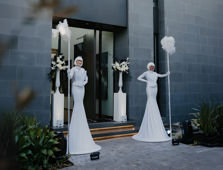 Hosts in white gowns welcoming guests at the entrance of a private event